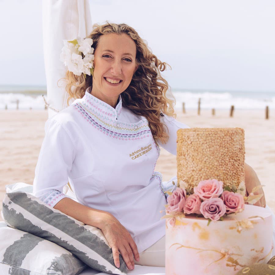 Adriana Bologna con su chaqueta blanca, sentada en la playa junto a un pastel decorado con rosas